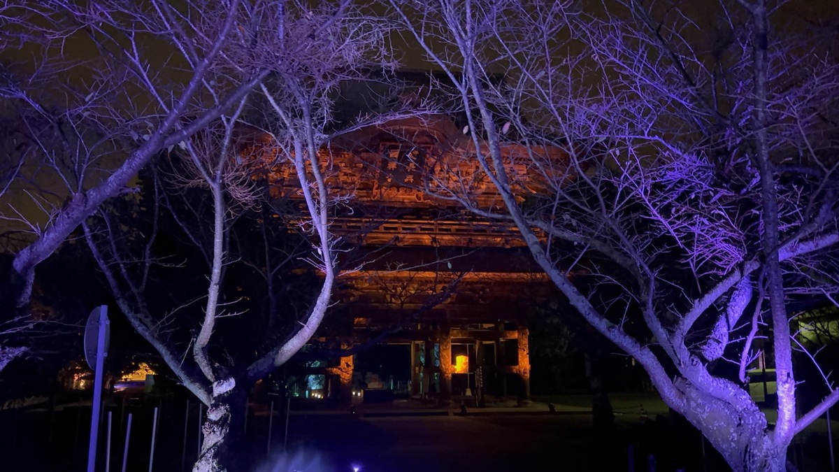 紫色の木々の奥に金色に浮かび上がる建長寺三門